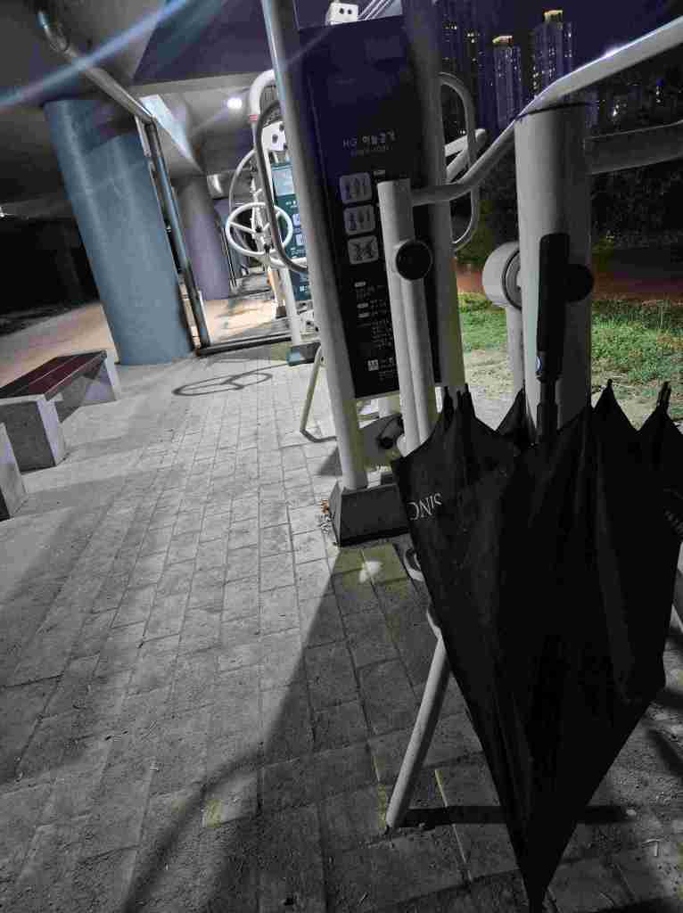 An umbrella left beside outdoor exercise equipment during a rainy night run.